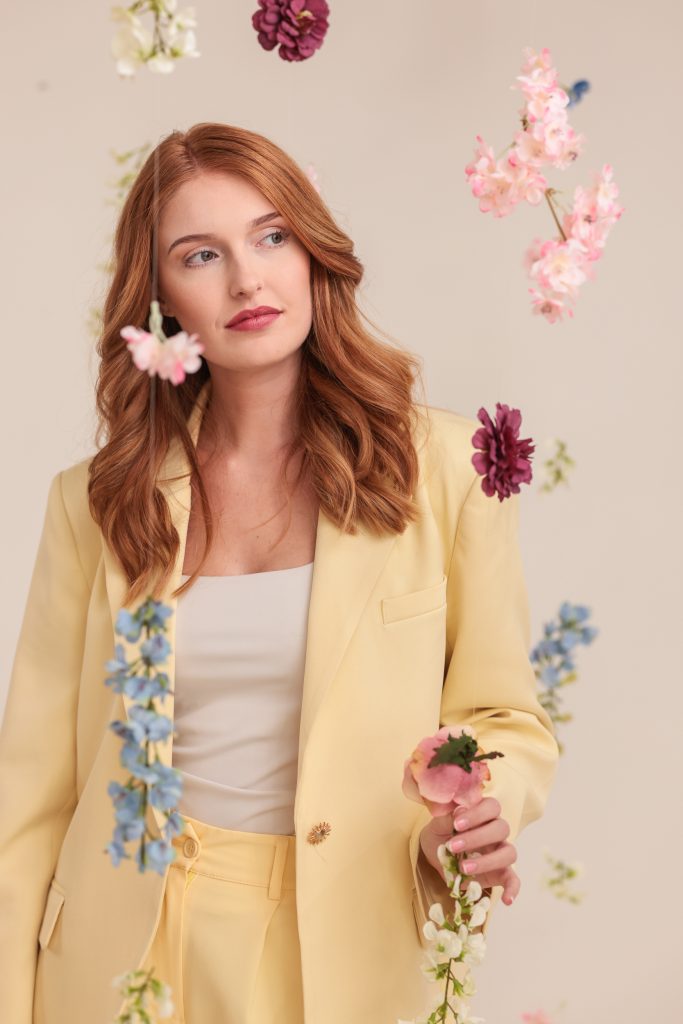 Editorial portret van een roodharige vrouw in bloemen decor in botergeel pak