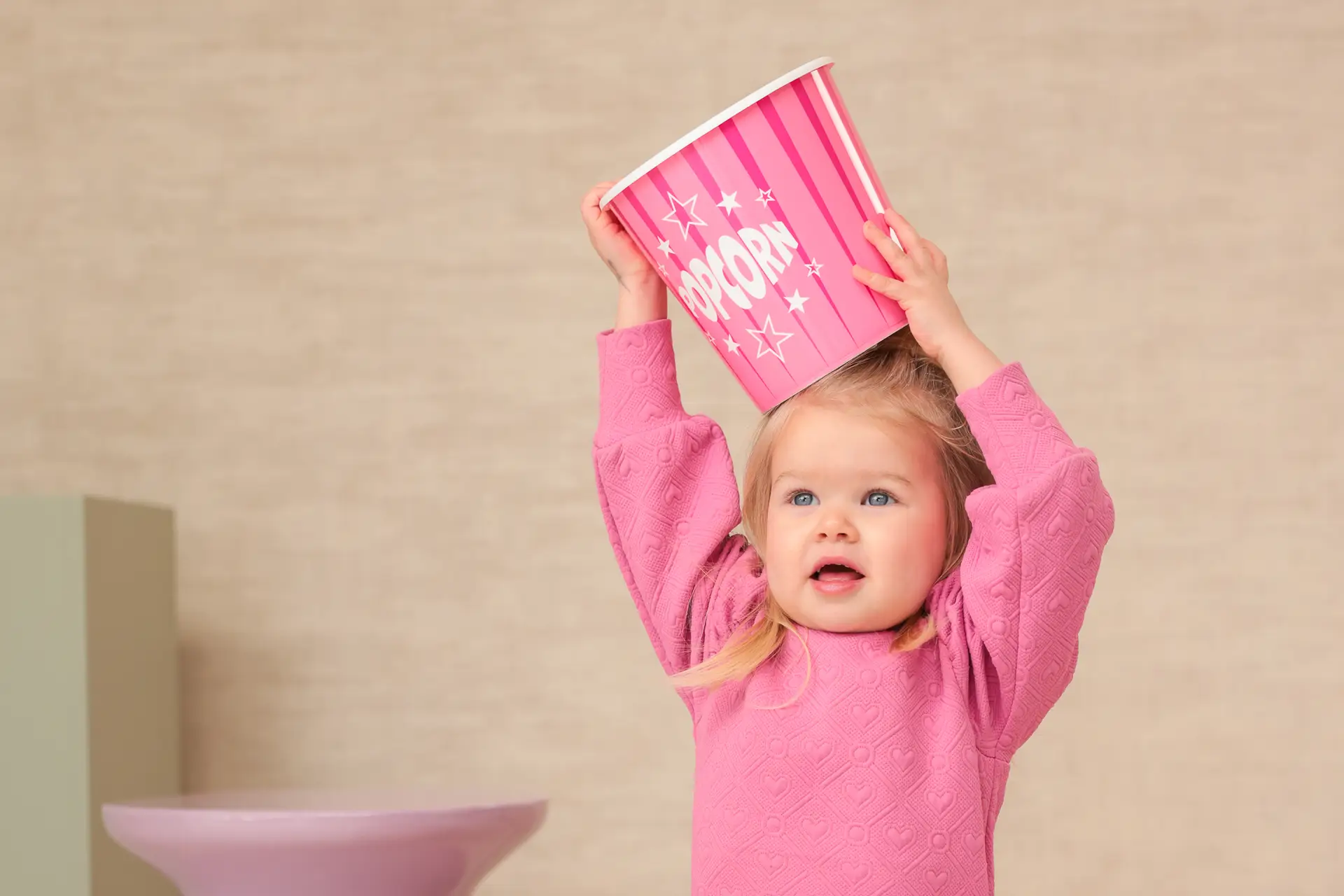 Peuter met een roze popcornemmer in een kleurrijke studio, speels en vrolijk beeld.