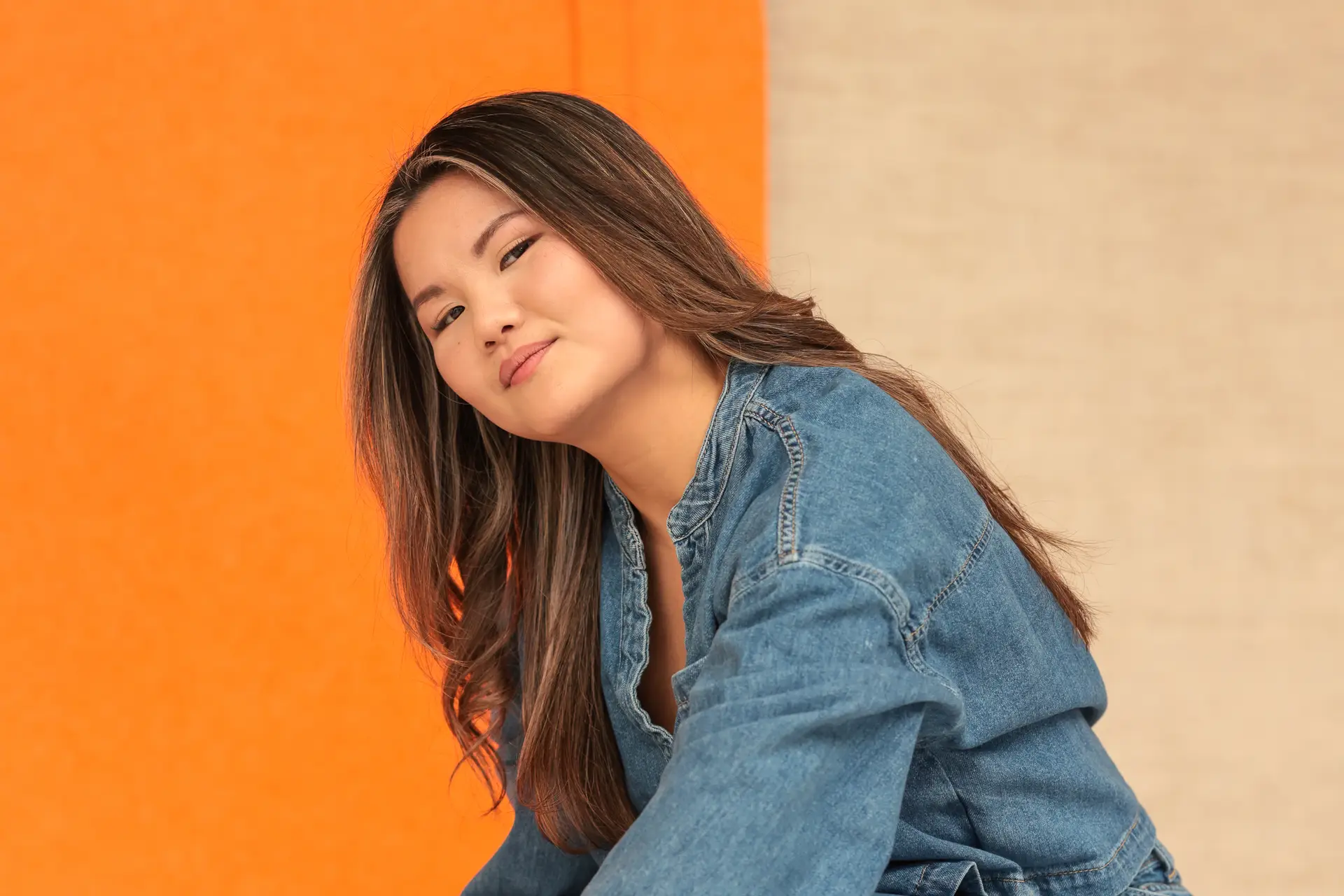 Portret van een vrouw in denim voor een oranje achtergrond in een daglichtstudio