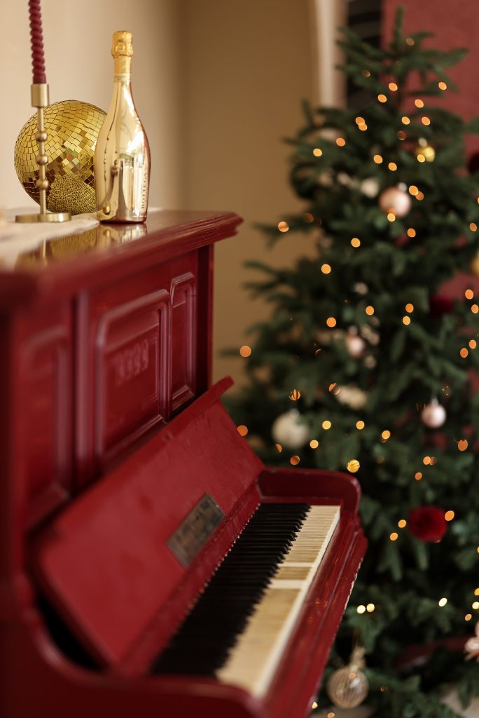 Rode piano met champagnefles en discobal, op de achtergrond versierde kerstboom met lichtjes in daglichtstudio Brabant