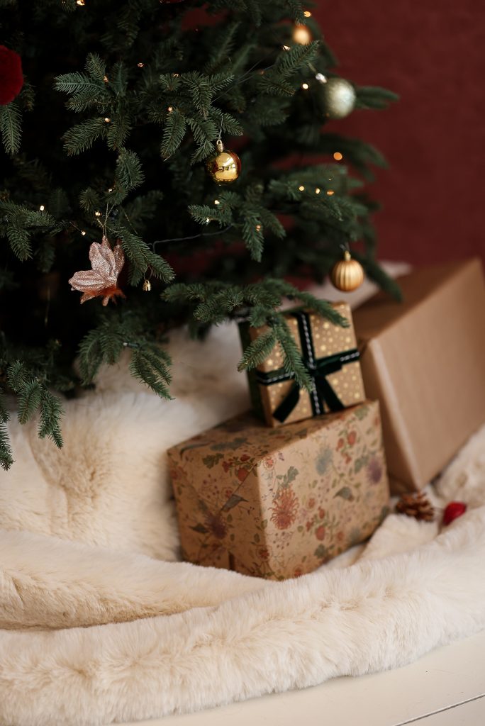 Een kerstboom met versieringen en verlichting, omringd door ingepakte cadeaus op een zachte witte ondergrond. Kerst in daglicht studio Roosendaal